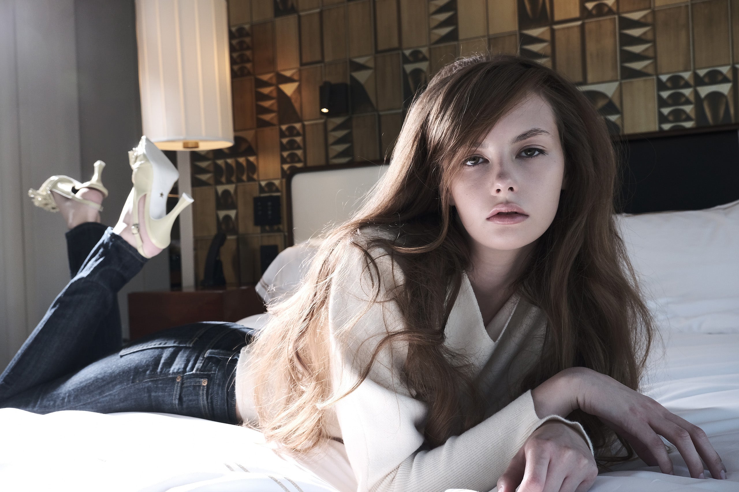 Woman lying on a bed holding high heels in a bedroom setting