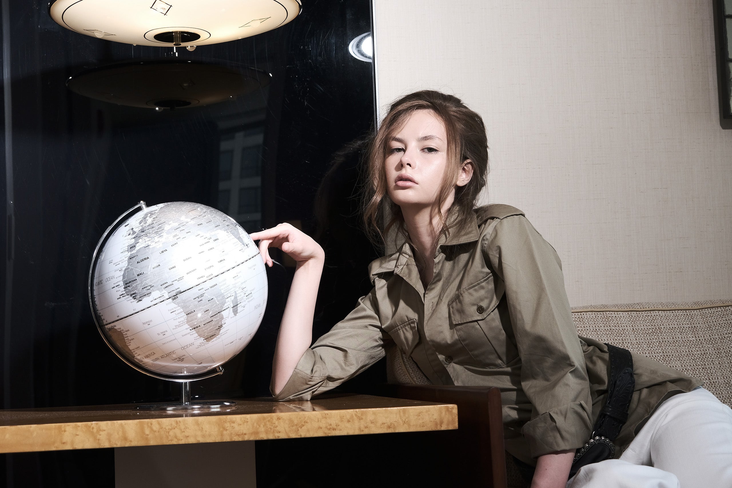 Woman in a green jacket sitting next to a world globe on a table.