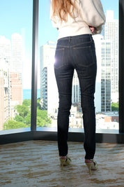 Person wearing dark jeans and high heels standing in front of a large window with cityscape view.