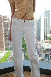 Person wearing a beige lace top and white pants with a cityscape background